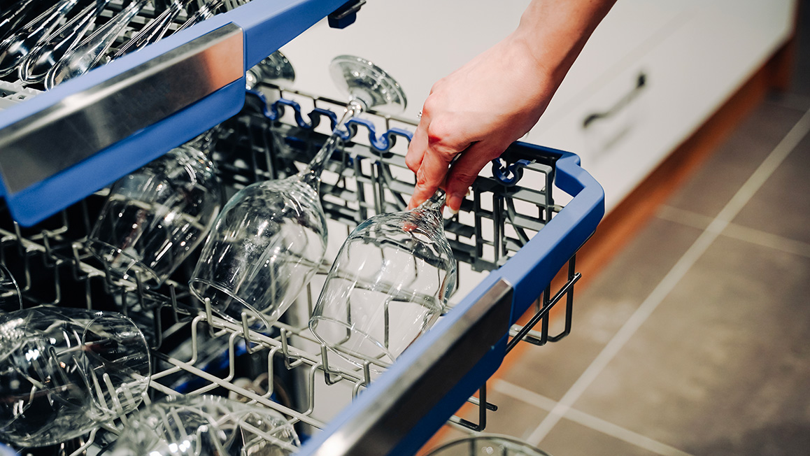 A person organizes dishes inside a dishwasher and prepares for a wash cycle in a tidy kitchen.