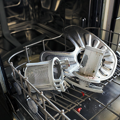The bottom rack of a dishwasher with a soiled filter resting in it.