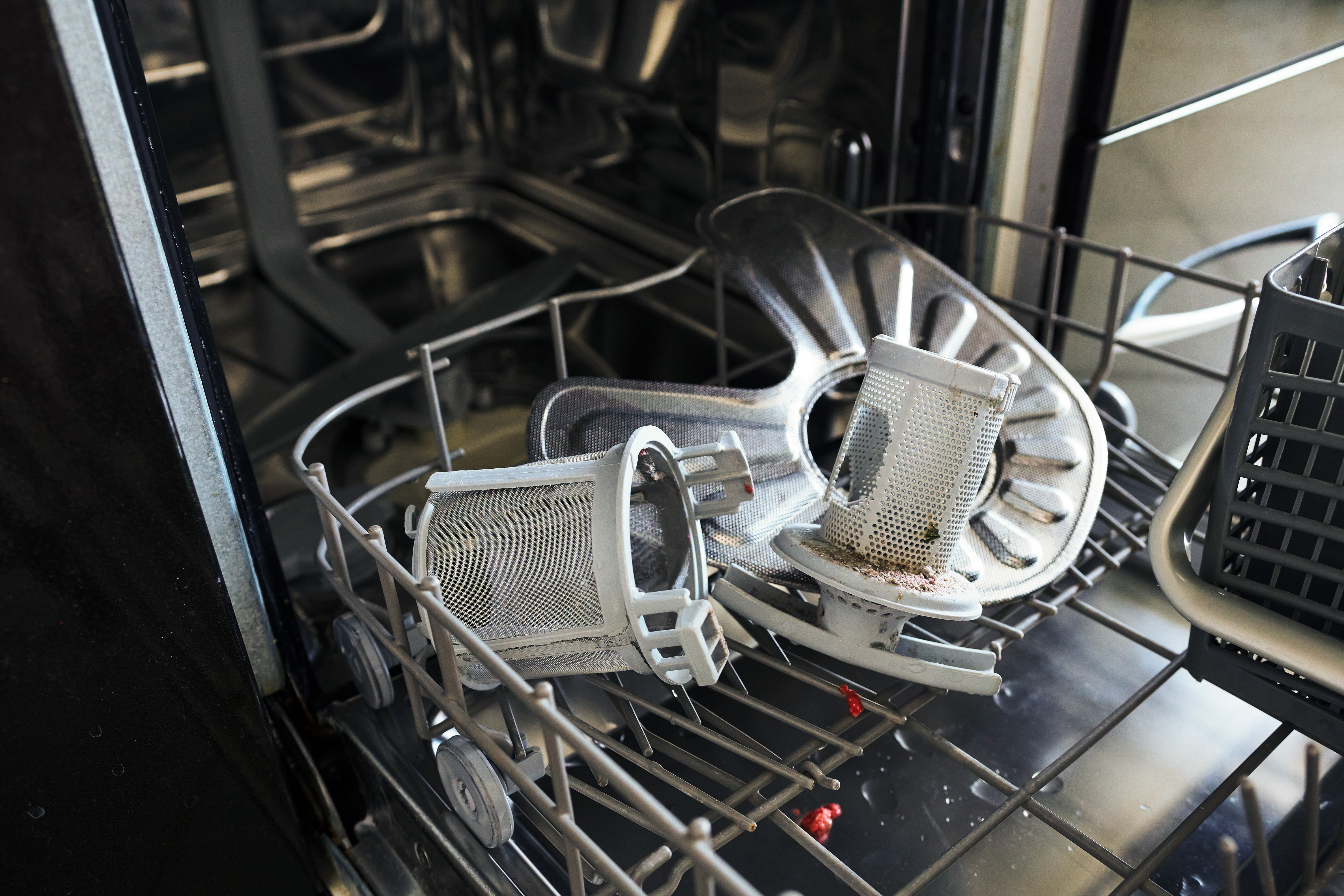 An open dishwasher with visible filters and a spray arm placed on the bottom rack.