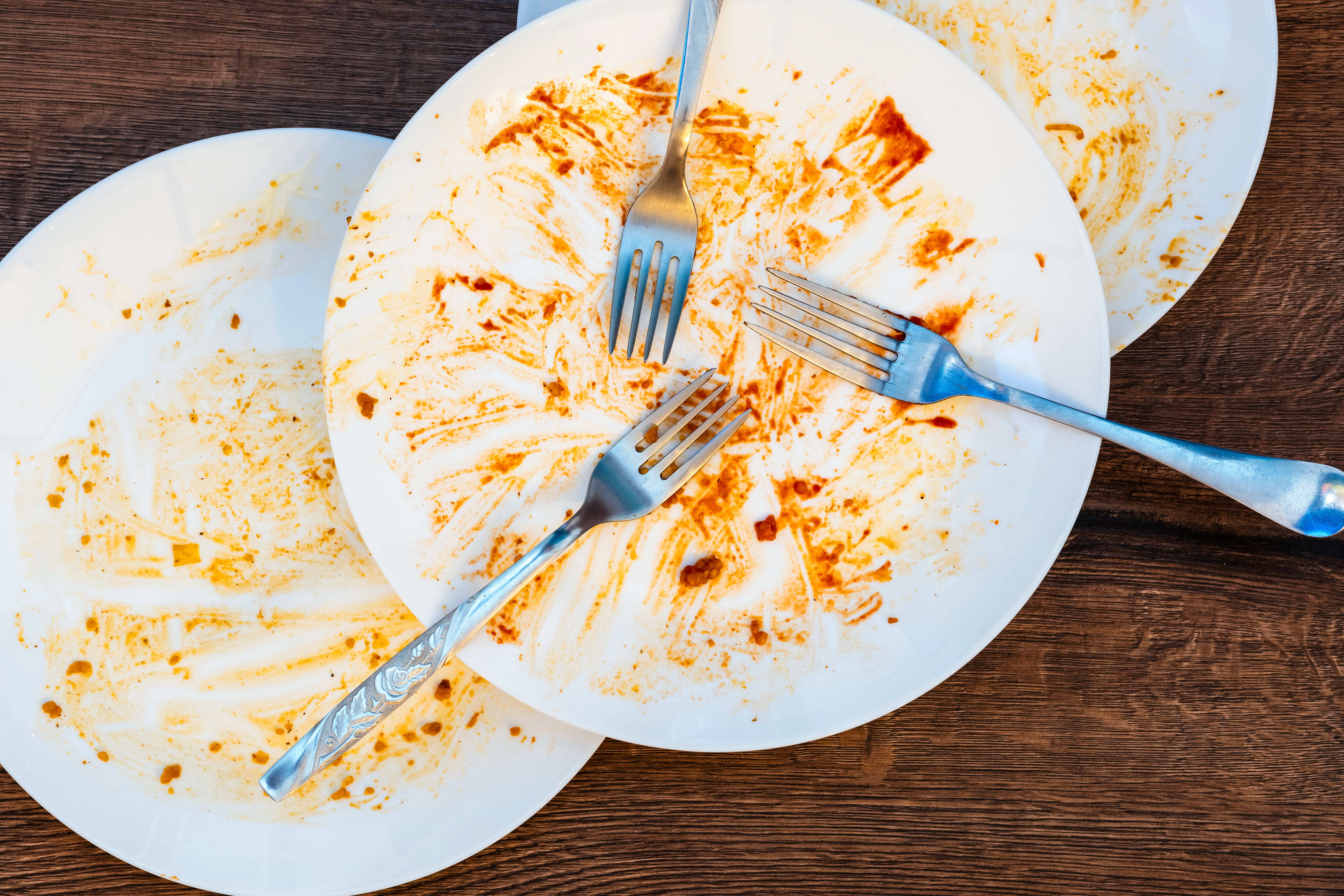 Three soiled white dishes with three soiled stainless steel dinner forks.