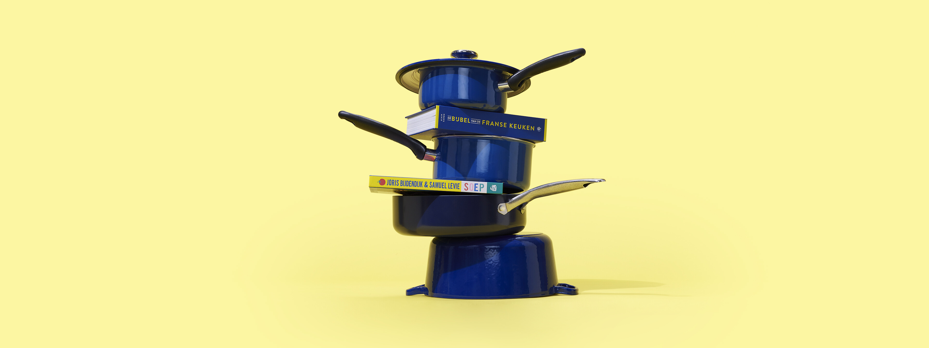 Stapel van blauwe pannen met daartussenin kookboeken
