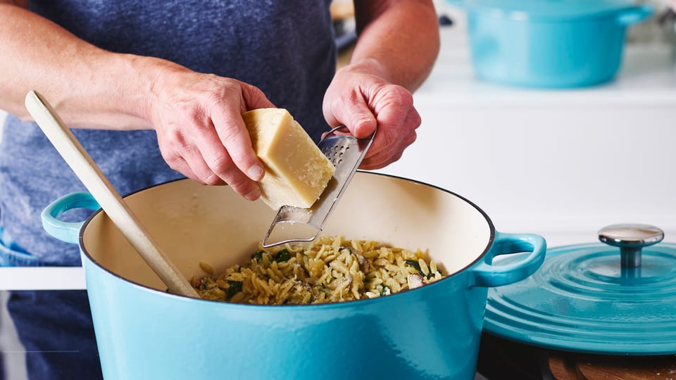 Persoon die kaas raspt boven een braadpan Persoon die kaas raspt boven een braadpan