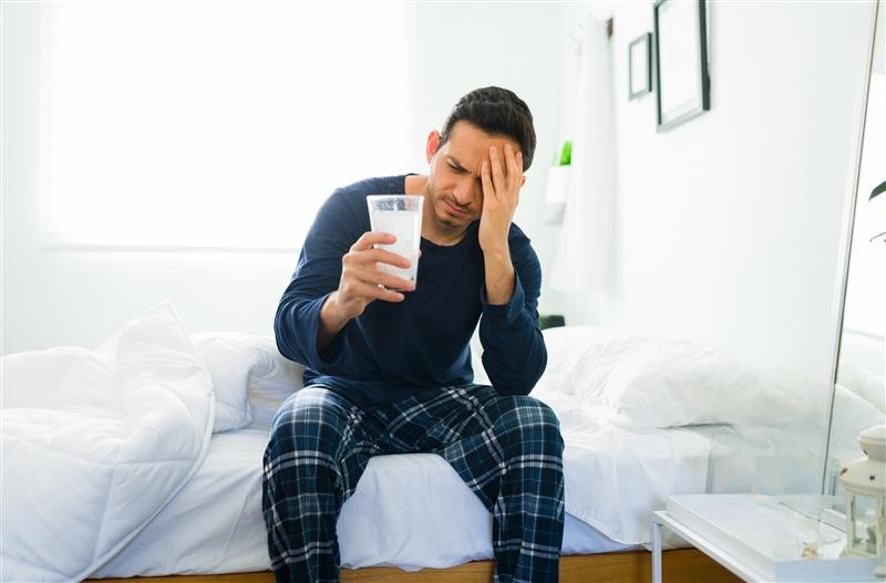 Hombre con cruda tomando un vaso con antiácido efervescente