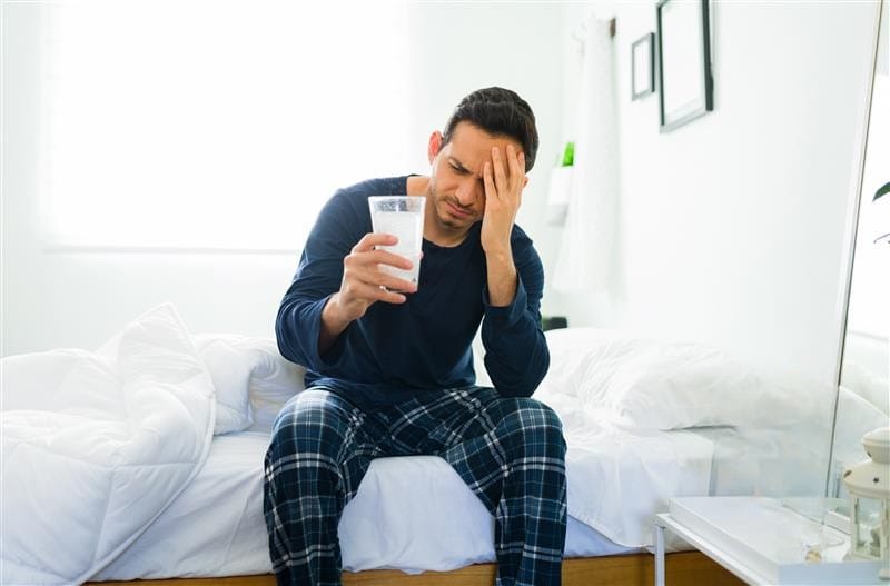 Hombre con cruda tomando un vaso con antiácido efervescente