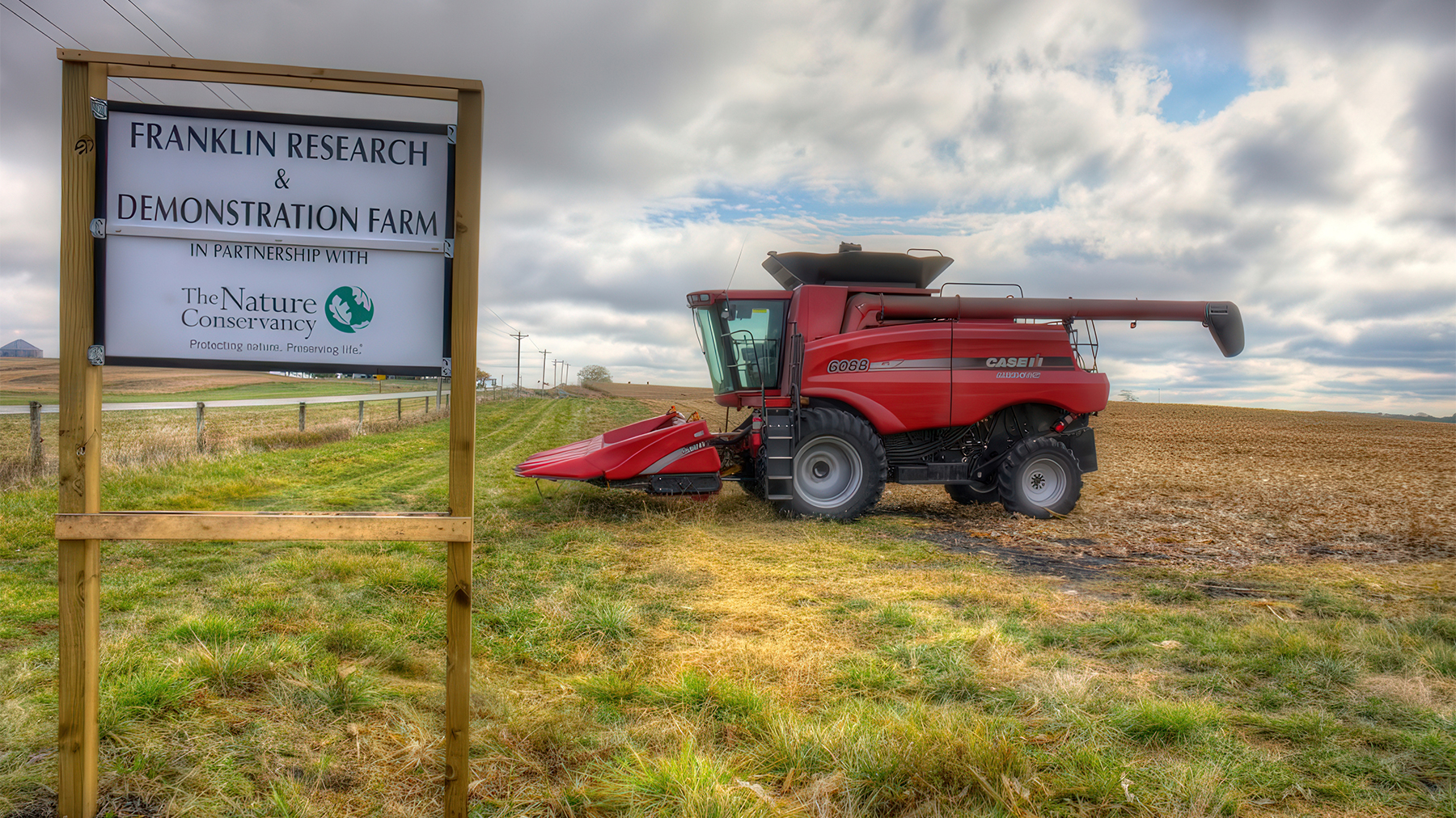 A Case IH combine parked in a field near a sign for a research and demonstration farm
