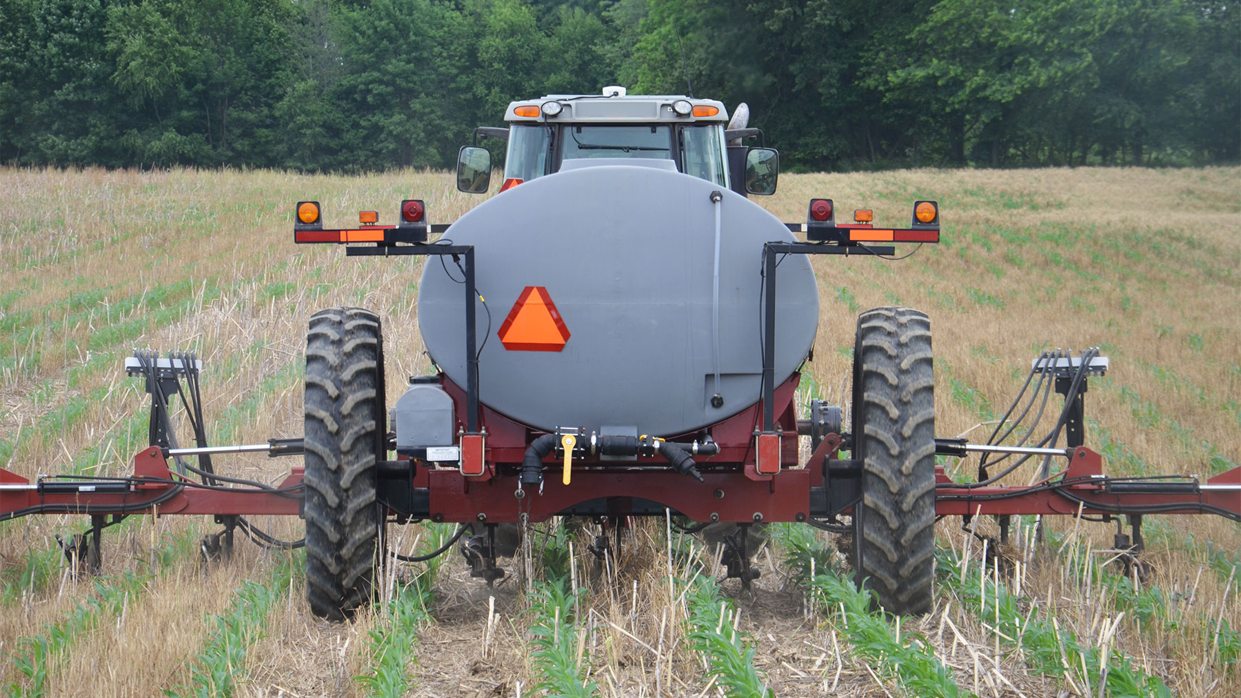 view from behind a of tractor pulling an anhydrous tank through a field and applying nitrogen